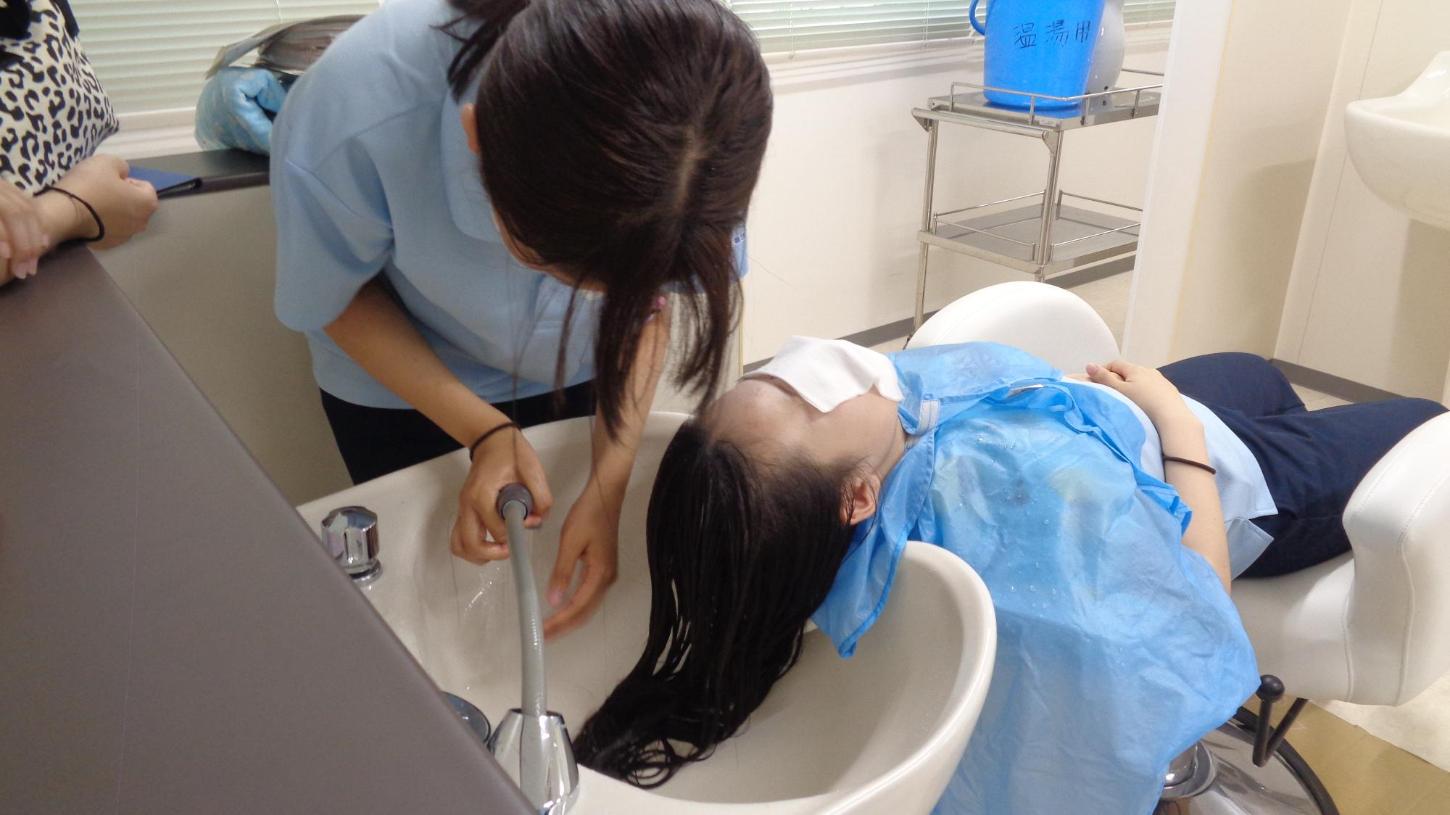 学生が洗髪台の前に仰向けに座った学生の洗髪をしているところの写真
