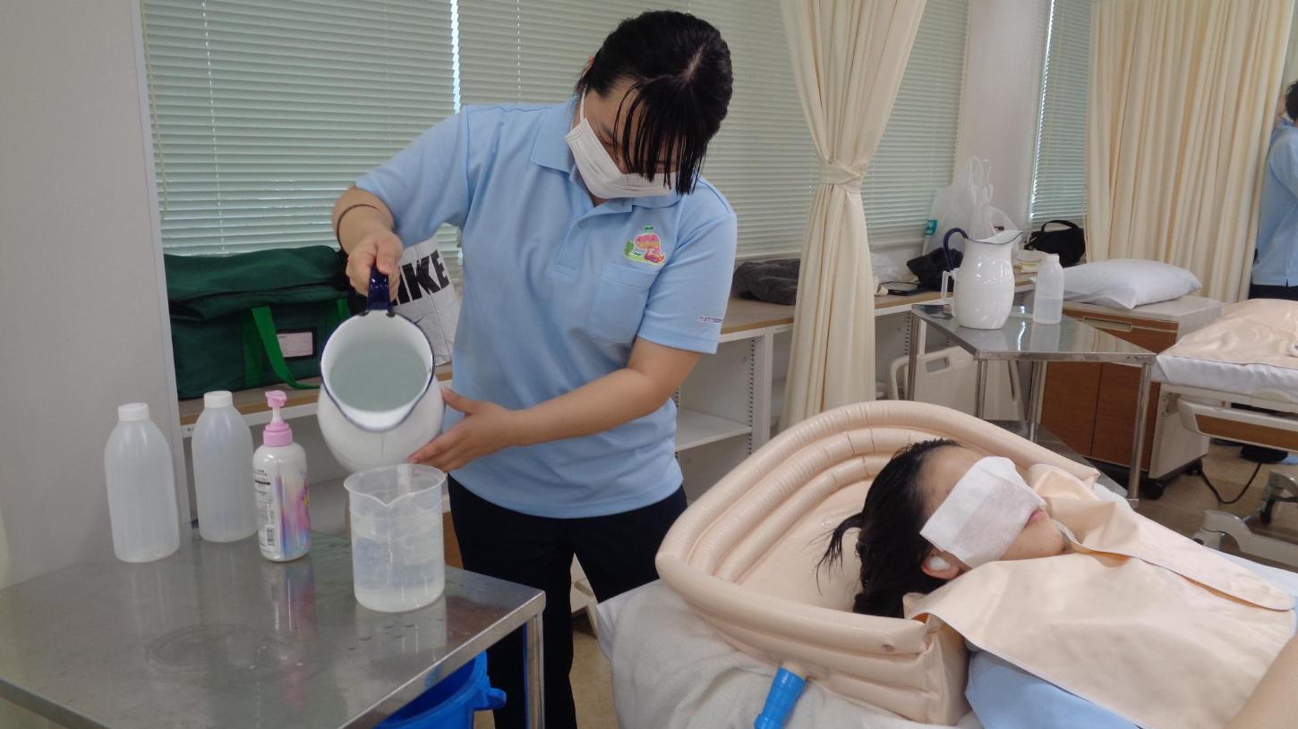 学生がベッド上で学生の洗髪をした後、ピッチャーの湯を準備しているところの写真