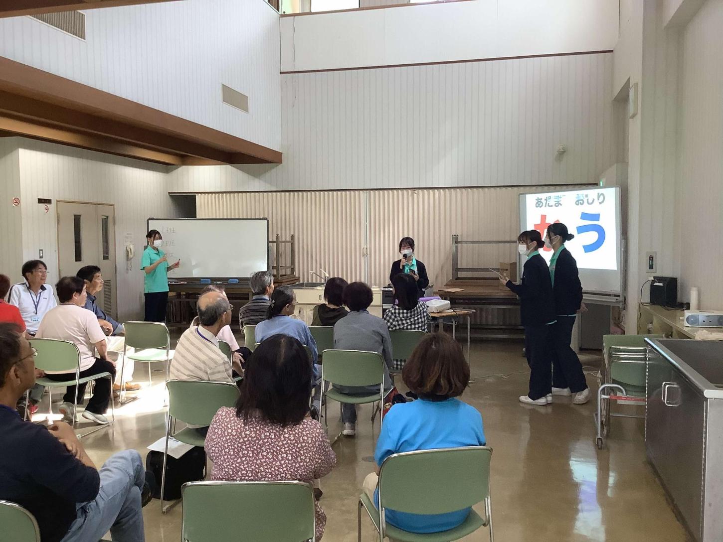 緑色のTシャツを着た学生4人がレクリエーションの説明をしている写真