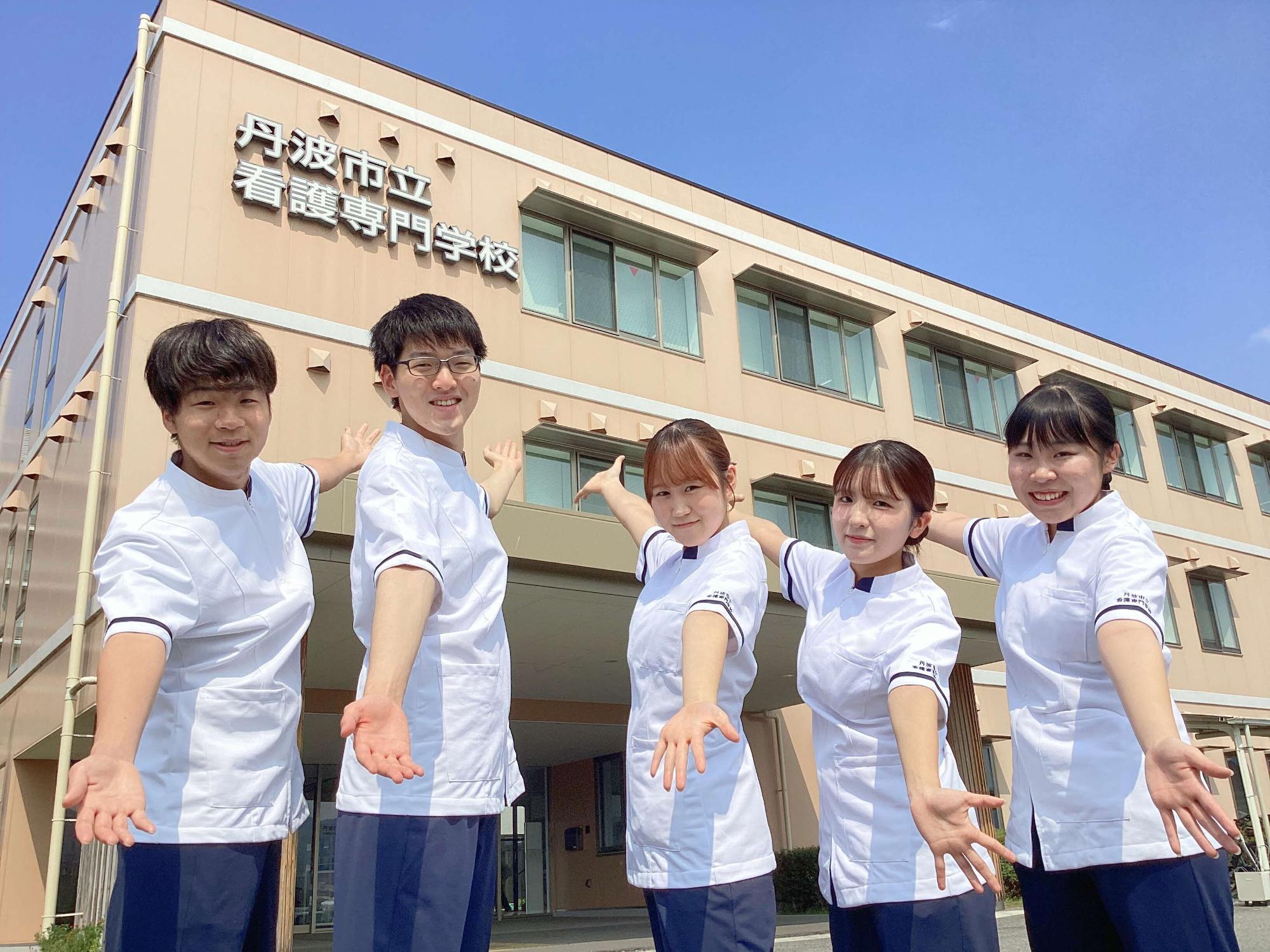 校舎の前で手を広げて笑顔の5人の学生たちの写真