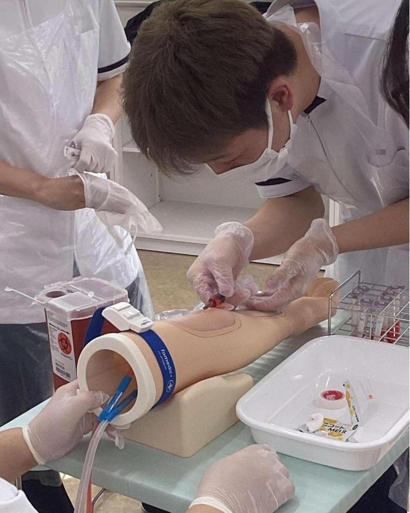 上腕モデルに注射器を刺して採血している学生の写真