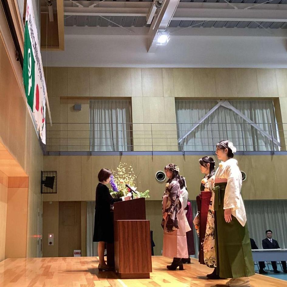 袴を着た卒業生4人が壇上で校長と向き合い、皆勤賞をいただいているところの写真