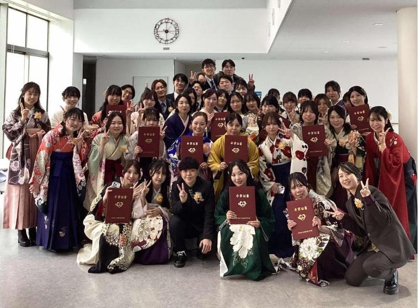 一階ロビーで卒業証書を持ってピースサインをしている卒業生の集合写真