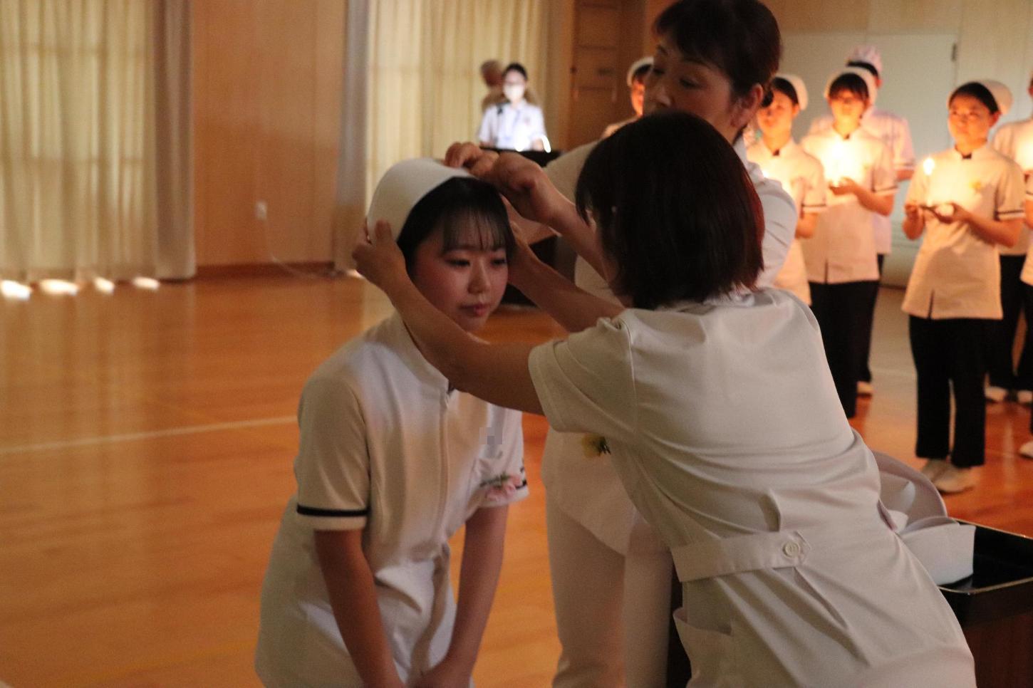 教員2人にナースキャップを頭にかぶせていただいている学生の写真