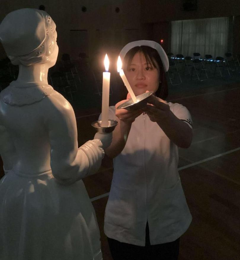 ナイチンゲール像が持つキャンドルに灯った火を学生が持つキャンドルへ火を移しているところの写真