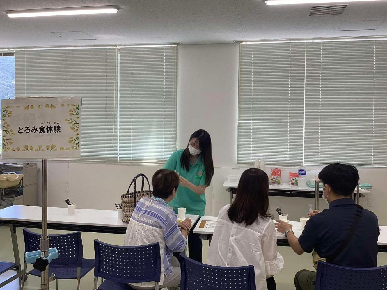 とろみ食の説明をしている学生とそれを聞いている参加者3人の写真