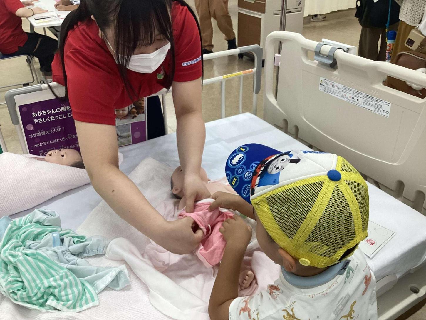 赤ちゃん人形の肌着を持って学生と一緒に着替えさせている子どもさんの写真