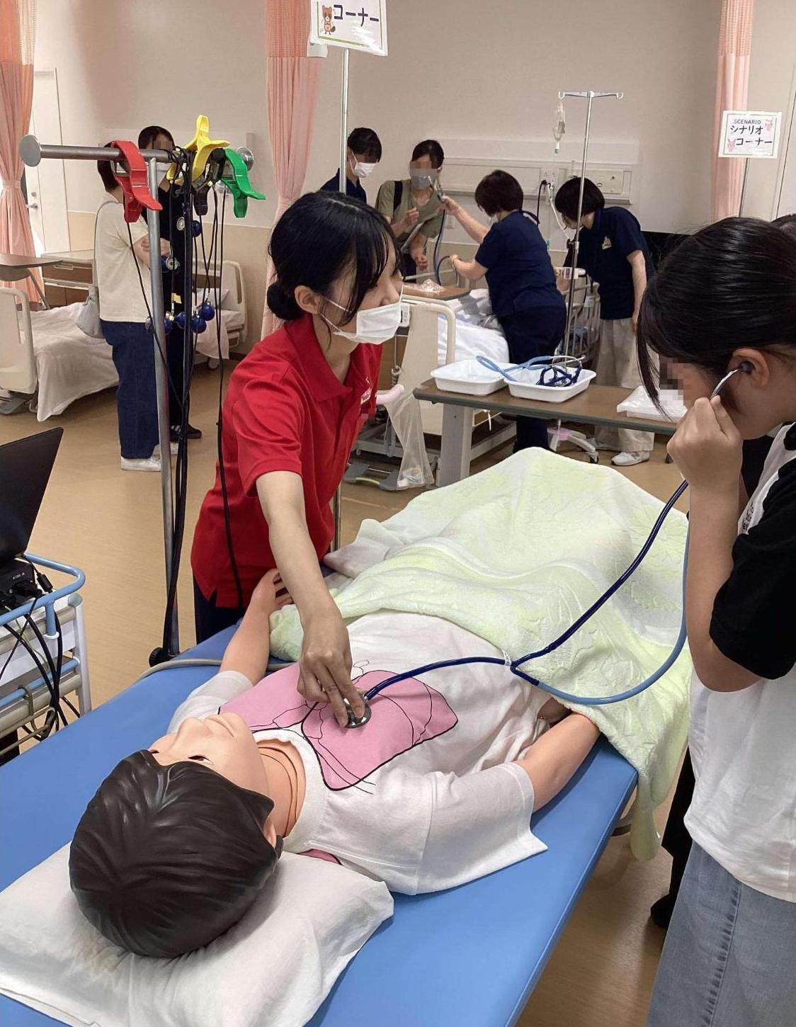実習室でシミュレーター人形の呼吸音や、設定した病状の肺の音を聞いている参加者たちの写真
