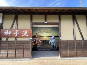 「御手洗」と書かれた看板のある日本家屋と、その入り口奥に武将2人のイラストポスターが貼られてる写真