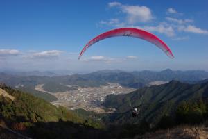 赤いパラグライダーが、麓の町並みを眺めながら山から空を下っていく写真