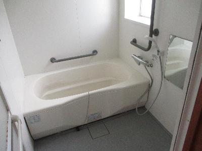 白を基調とした浴室で、グレーの床と2か所に手すりがある写真