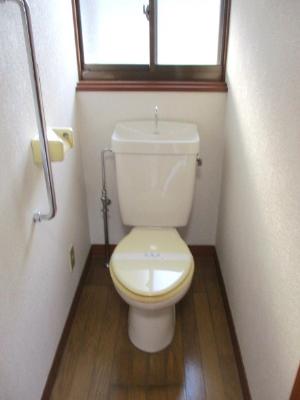 奥の上部に窓があり、フローリングの床で白を基調としたトイレの写真
