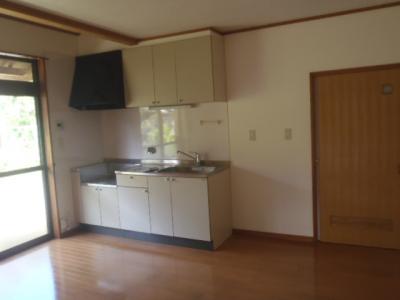 左奥に白いキッチンスペースがあるフローリングの部屋の写真