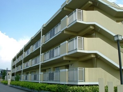 薄い緑の混じった茶色の3階建てのマンションとそれに面している道路の写真