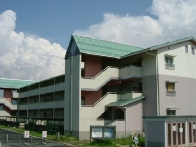 前に駐輪場がある外壁が白い3階建ての建物の写真