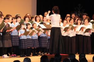合唱をする子供たちや女性を指揮する指揮者の写真