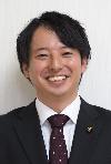 黒いスーツにえんじ色のネクタイをした黒髪の男性の写真