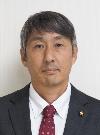 黒いスーツにえんじ色のネクタイをしたグレーの髪の男性の写真