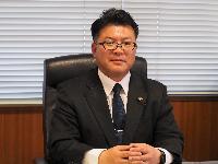 黒のスイーツに紺色のネクタイを着けて眼鏡をかけた男性の写真