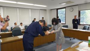 女性が男性に報告書を手渡し、男性が一礼しながら受け取っている写真
