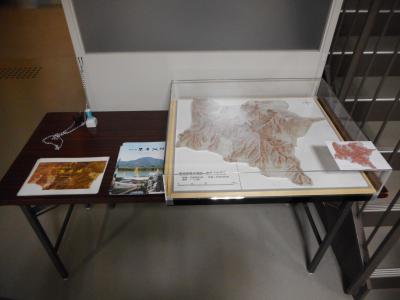 机の上に置かれたスタンプとパンフレット、ショーケースの中に入った立体模型の写真