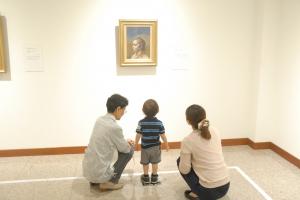 壁にかけられた展示物を見上げて眺めている子供と付き添っている親の写真