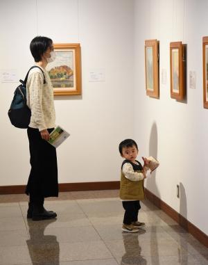 壁の展示物を見ている親と、カメラ目線になっている子供の写真