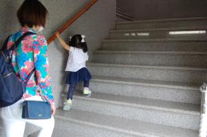 子供が手すりを掴んで階段を登り、それを見守っている親の写真