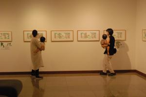 赤ちゃんを抱っこしている母親2人組が壁にかけられた展示物を眺めている写真