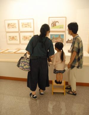 親と台に乗った子供がショーケース内の絵画を一緒に見ている写真