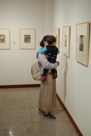 母親に抱き抱えられた子供と一緒に壁にかかった展示物を見ている写真