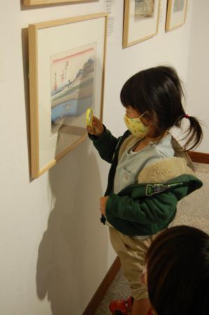 壁の展示物を黄色い虫眼鏡越しに見ている子供の写真