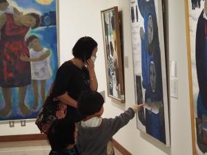 壁にかかった展示物に指さしている子供と展示品を見ている親の写真