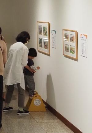 壁の展示物前に置かれた台に乗ろうとしている親子の写真