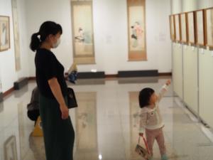 壁に並んで展示された絵画を指差す小さな女の子と、付き添う女性の写真