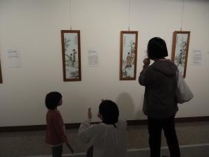 壁に展示された3つの縦長の版画を鑑賞する親子達の写真