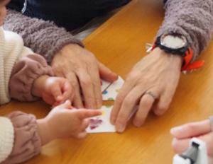 カラフルな図形が描かれたカードのパズルを揃える大人の手と、小さな子どもの手の写真