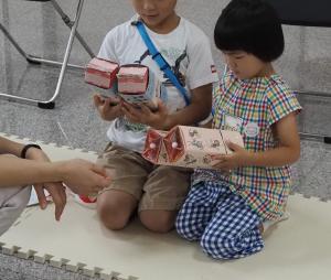 牛乳パックを二つ繋げた形のからくり絵本を手に持った二人の子どもの写真