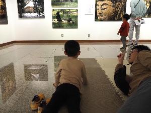 小さな男の子がお父さんと床に寝そべって壁の作品を見ています