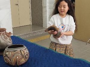 子どもが両手で土器を運んでいます。