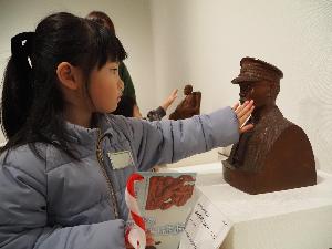 女の子が人物彫刻作品の頬を撫でています。