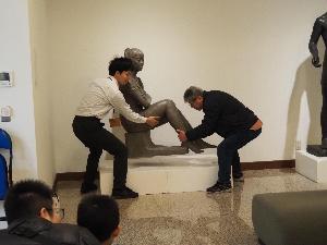 男性が二人で彫刻作品を持ち上げています。