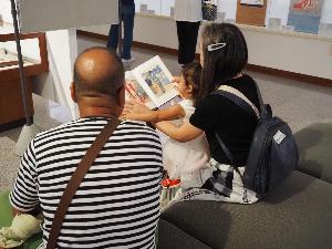 女の子が祖父母と一緒に展覧会図録を見ています
