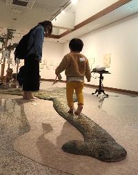 小さな男の子が丹波竜の作品の上をはだしで歩いています。