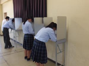女子生徒と男子生徒が記載台で投票用紙を記入している写真